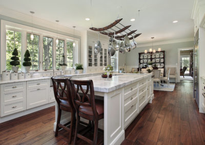 Bright and modern renovated kitchen with white shaker panel cabinets and sleek finishes. The kitchen features a large center island with seating, perfect for entertaining. The open concept design allows for easy movement and socializing while cooking. The natural light and white color scheme give the space a fresh and airy feel