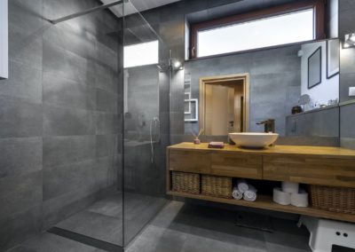 Stylish grey bathroom with sleek finishes and modern amenities. The grey color scheme adds a touch of sophistication, while the renovated fixtures and finishes create a luxurious spa-like atmosphere. Features include a glass shower enclosure and wooden vanity