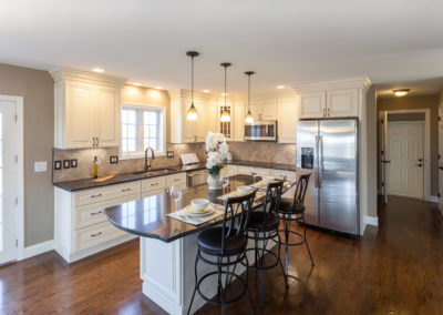 Bright and modern renovated kitchen with white shaker panel cabinets and sleek finishes. The kitchen features a large center island with seating, perfect for entertaining. The open concept design allows for easy movement and socializing while cooking. The natural light and white color scheme give the space a fresh and airy feel