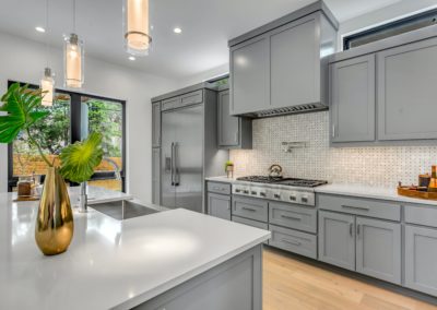 Elegant renovated kitchen with grey shaker panel cabinets and sleek finishes. The kitchen features a large center island with seating and a modern backsplash. The open concept design allows for easy movement and socializing while cooking. The grey color scheme and natural light give the space a sophisticated and modern feel