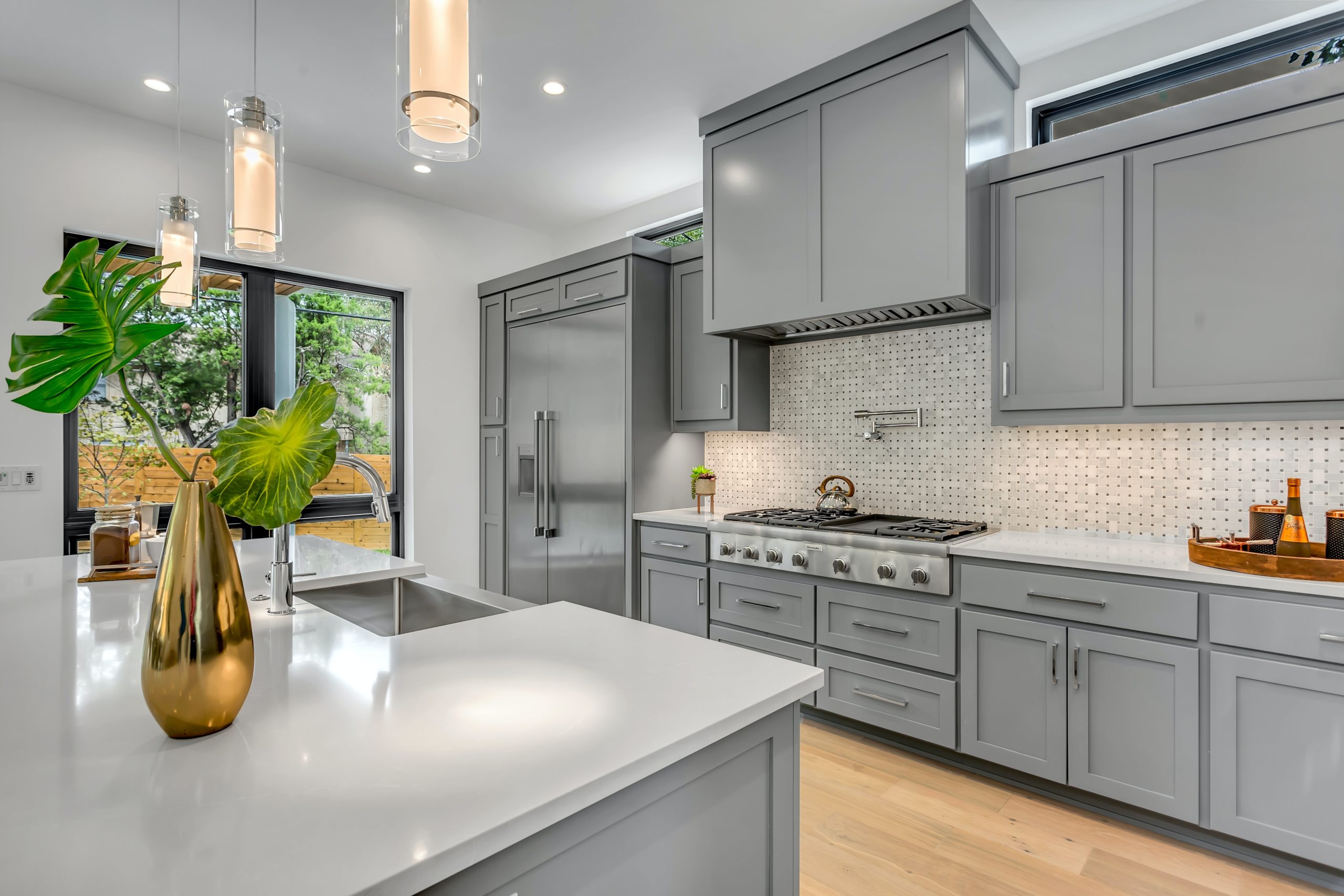 Elegant renovated kitchen with grey shaker panel cabinets and sleek finishes. The kitchen features a large center island with seating and a modern backsplash. The open concept design allows for easy movement and socializing while cooking. The grey color scheme and natural light give the space a sophisticated and modern feel