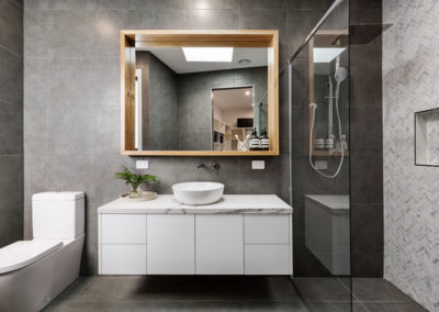 Modern designer bathroom with herringbone shower tiling and sleek white custom made vanity