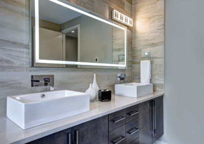 Contemporary master bathroom features a dark vanity cabinet fitted with rectangular his and hers sink and modern wall mount faucets under large mirror.