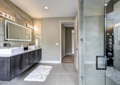 Contemporary master bathroom features a dark vanity cabinet fitted with rectangular his and hers sink and glass walk-in shower.