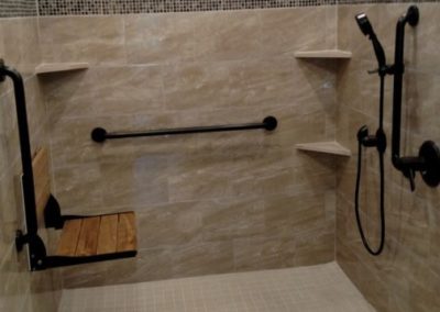 Renovated bathroom with accessibility features for disabled persons. The bathroom features a walk-in shower with a built-in bench and handrails