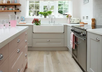 Stylish renovated kitchen with light grey shaker panel cabinets and a baby pink center island. The open concept design and natural light create a spacious and inviting atmosphere. The light grey and baby pink color scheme adds a modern and feminine touch to the space, perfect for entertaining or relaxing with family. Features include new appliances and sleek quartz countertops